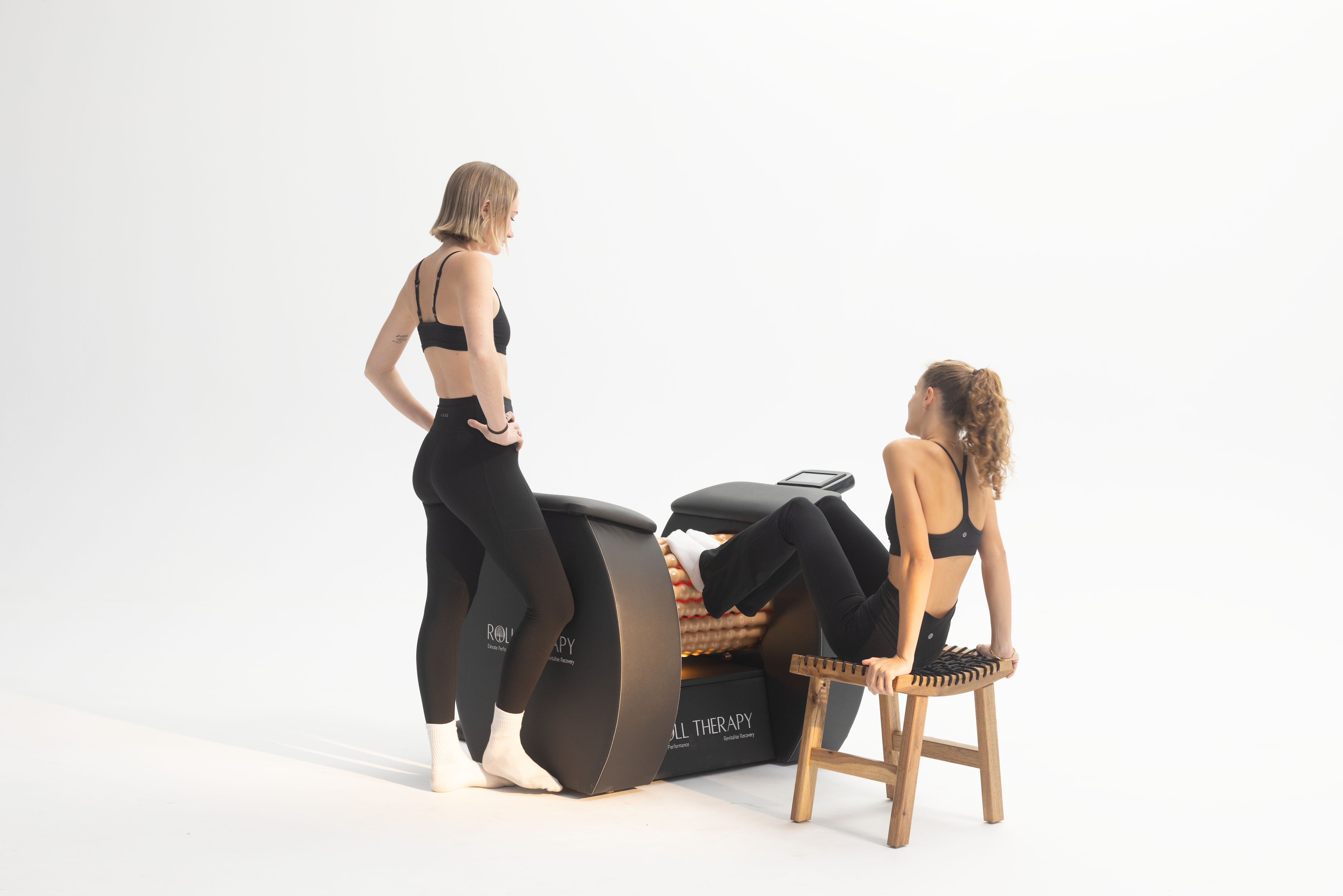 Two women using Roll Therapy lymphatic drainage machine - body rolling session for muscle recovery and circulation